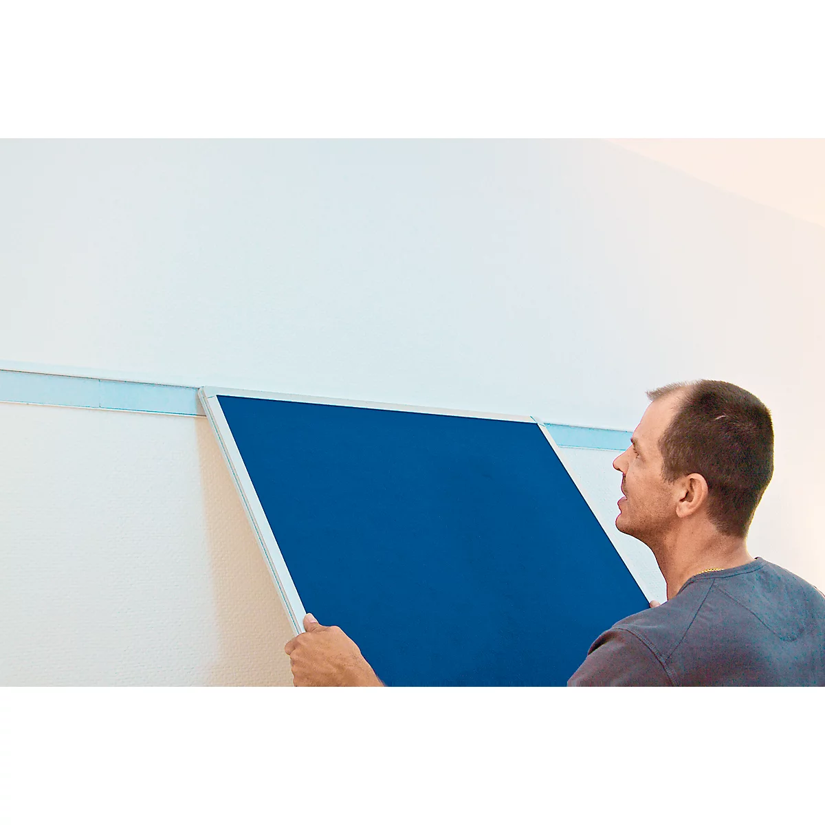 A man attaching a blue board to a wall fitted with a silver rail.