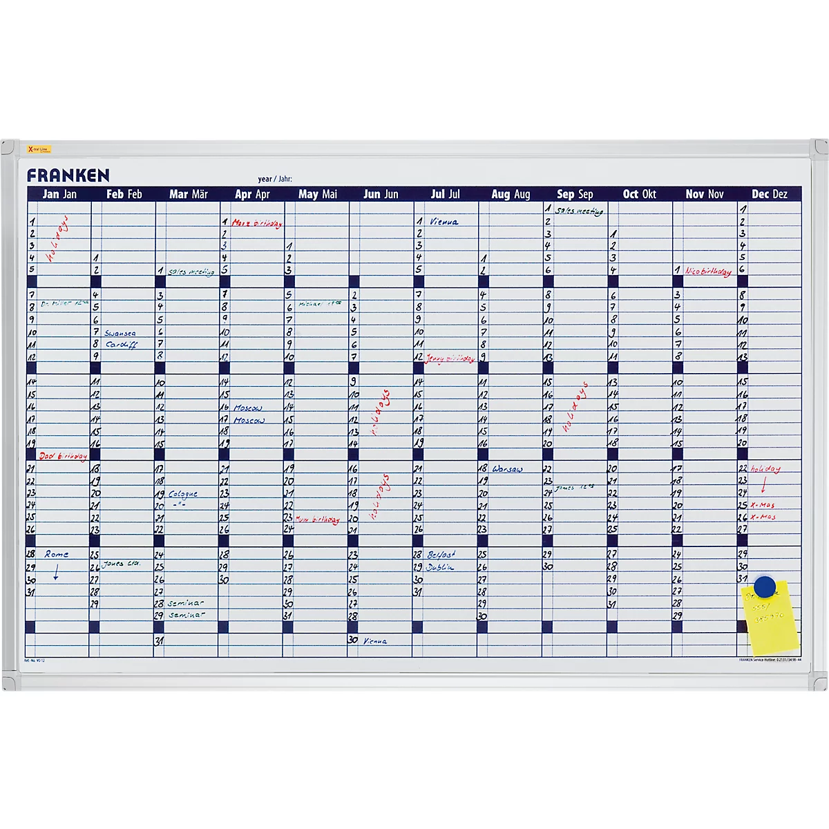 White annual planner board with markings and labels. On yellow note with pin.