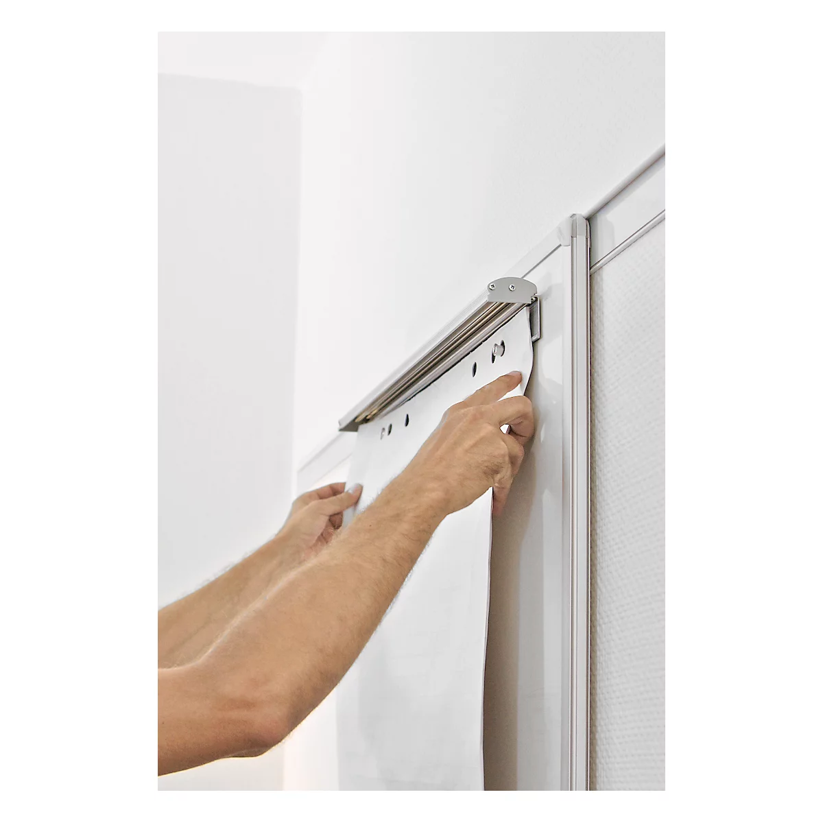 Hands attaching white fabric to bracket. Grey bracket on white wall. Few bore holes on the fabric recognizable.