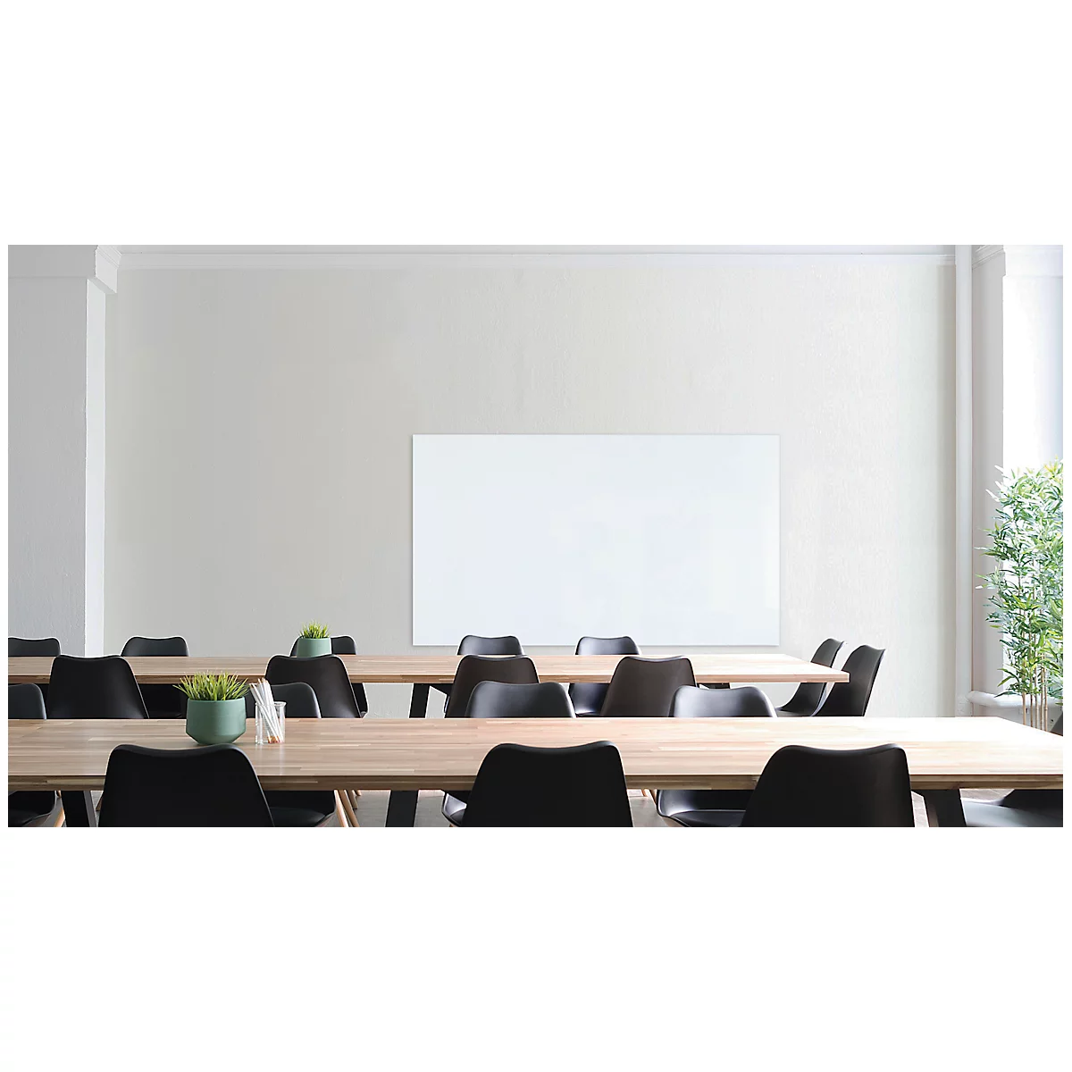 Conference room with wooden tables, black chairs, white board and plant decoration.
