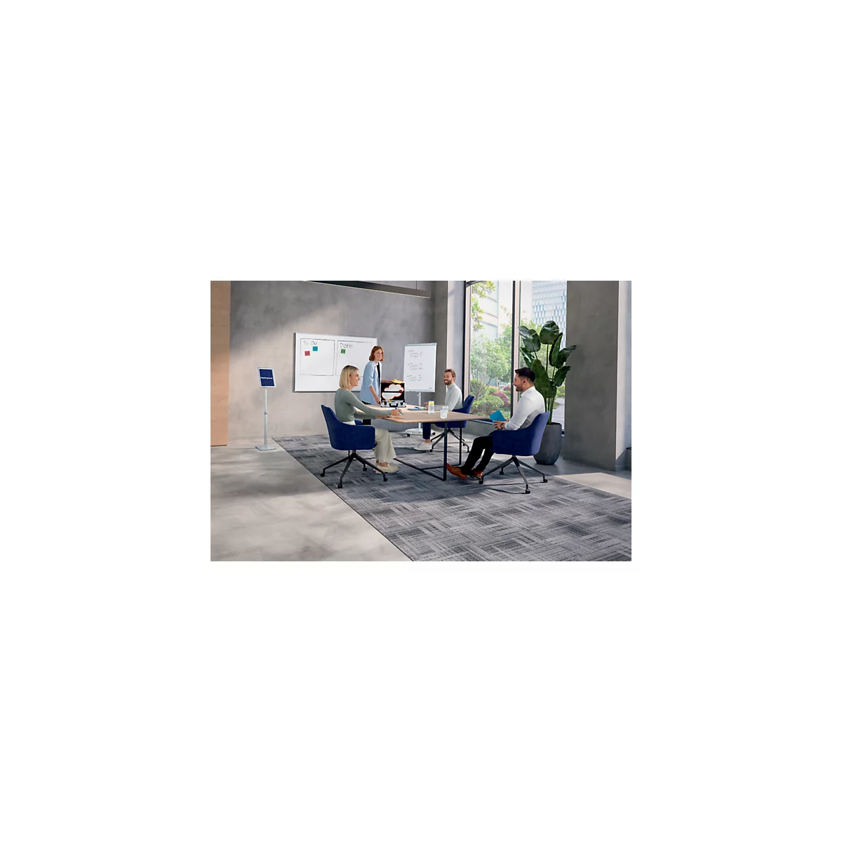Team vergadert aan tafel, er wordt gediscussieerd. Een flip-over en een whiteboard zijn op de achtergrond te zien.