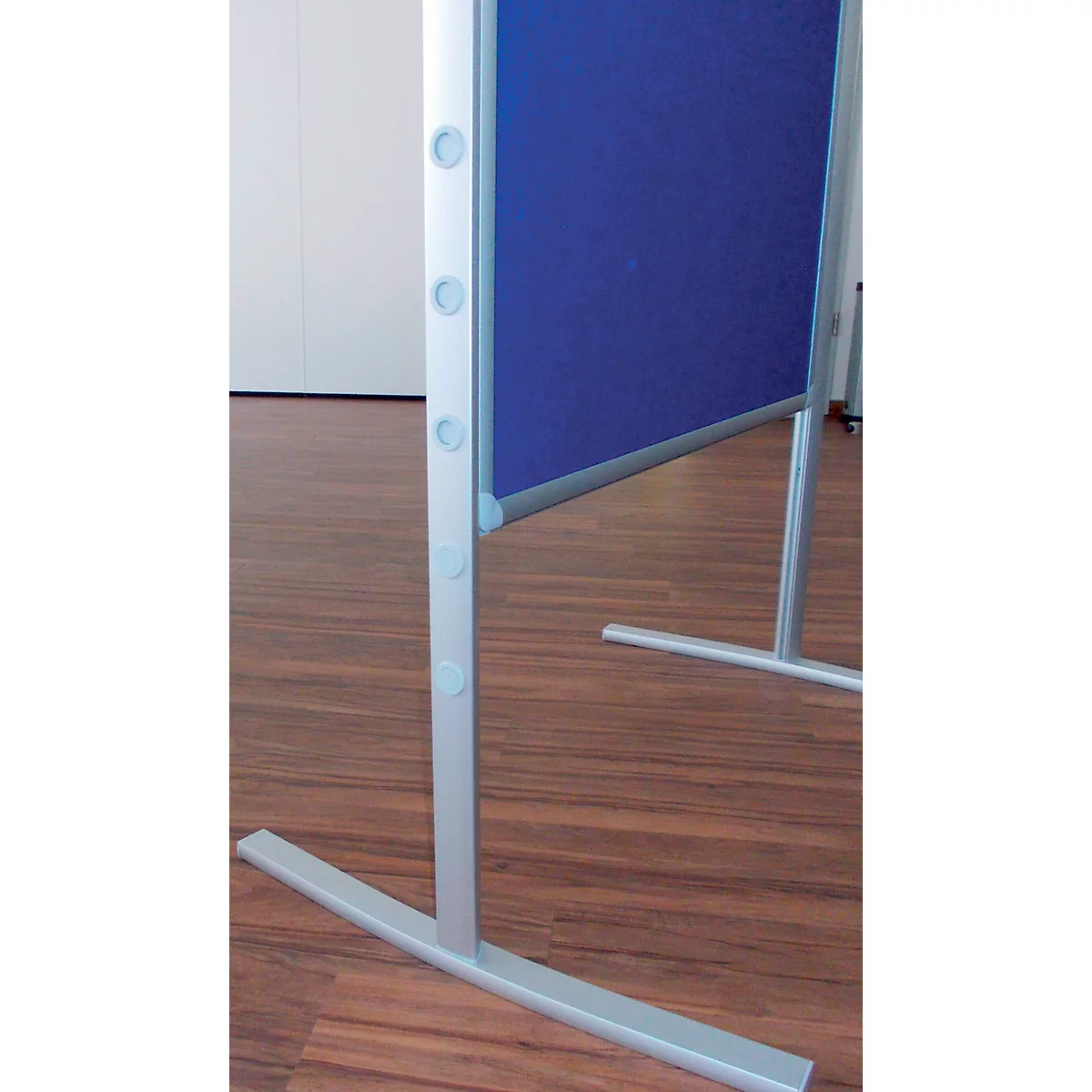 Close-up of a pinboard stand: silver metal frame with blue fabric, on a brown wooden floor.