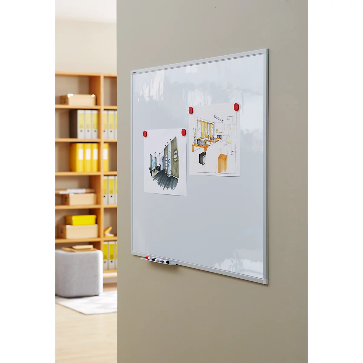 A white board with drawings and magnets on a wall. A shelf on the left, a beige wall on the right.