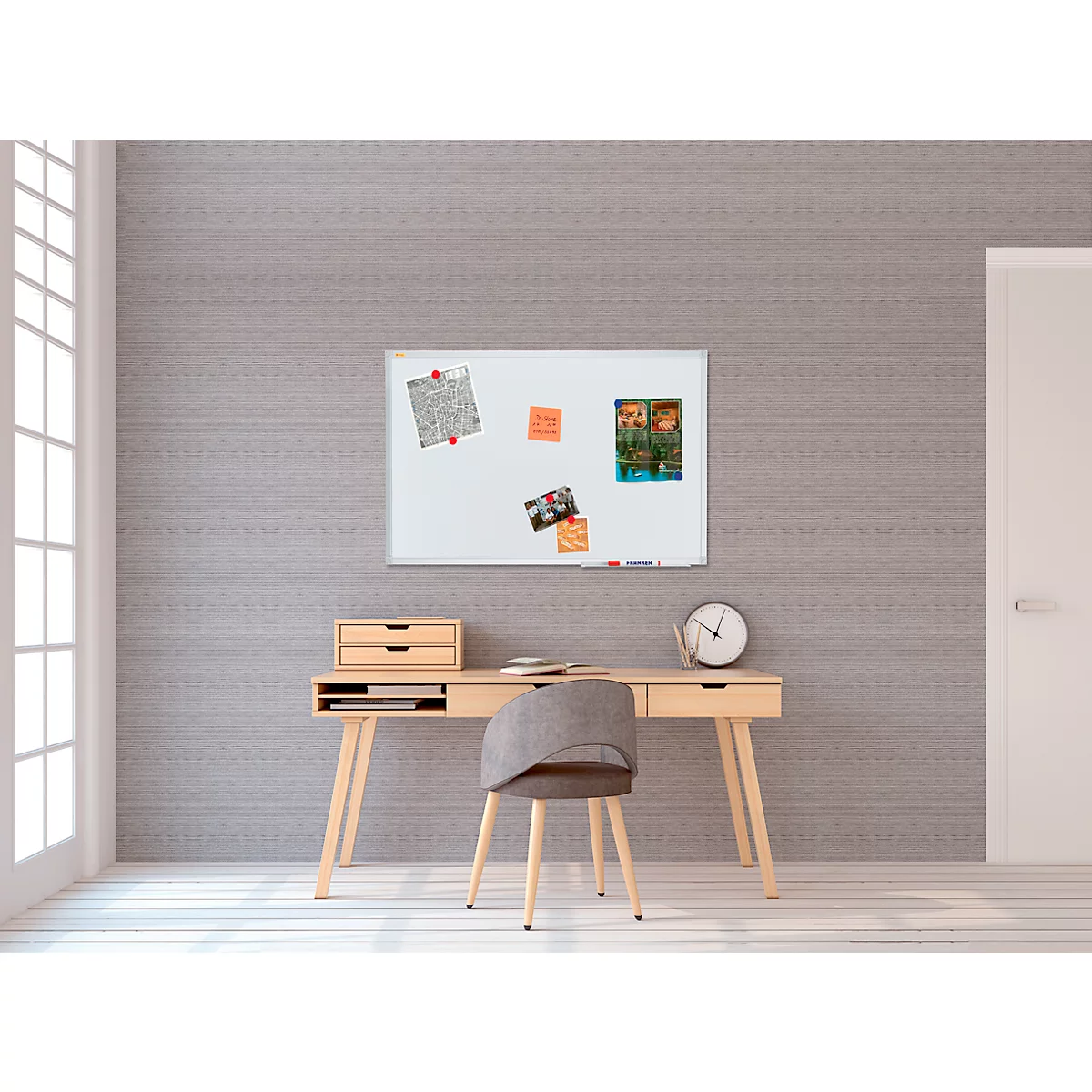 Desk with chair, whiteboard and clock in front of gray wall. Notes and photos on the whiteboard.