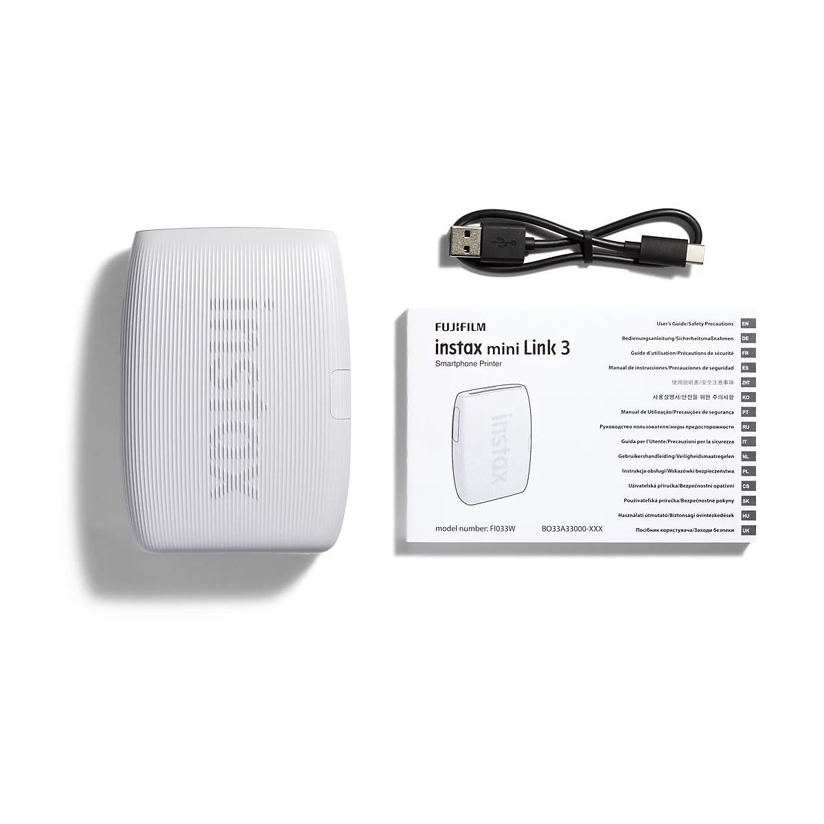Auf weißem Hintergrund liegen eine weiße Instax Mini Link 3 Smartphone Drucker, ein Ladekabel und eine Broschüre.