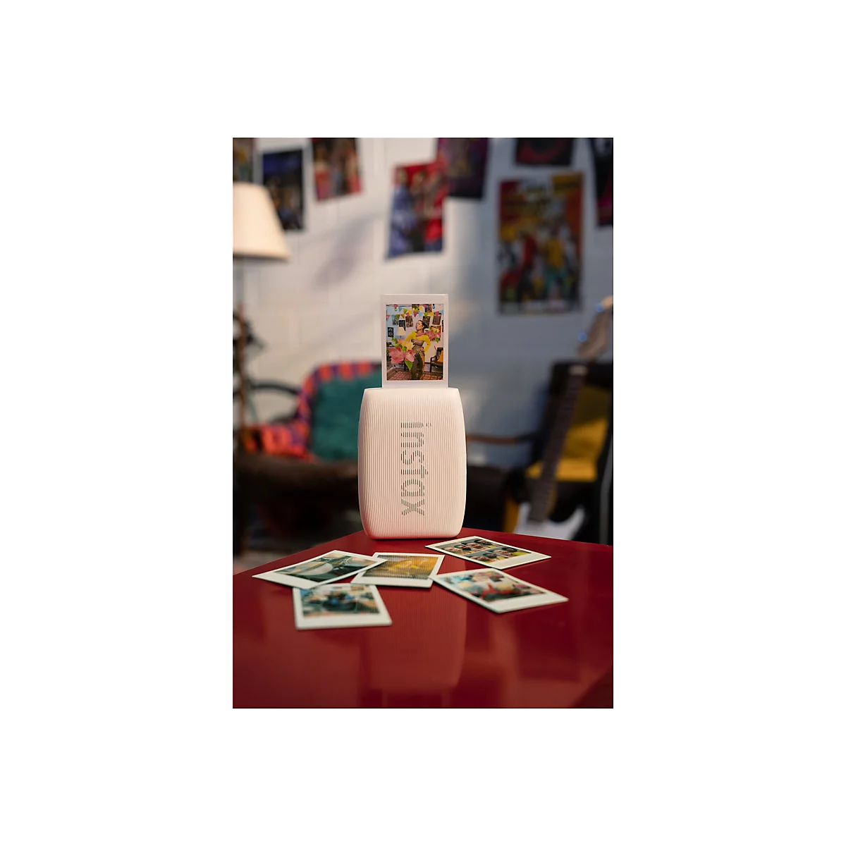 Rosafarbener Instax-Drucker, der ein Foto ausdruckt. Darunter liegen ausgedruckte Fotos auf einem roten Tisch.
