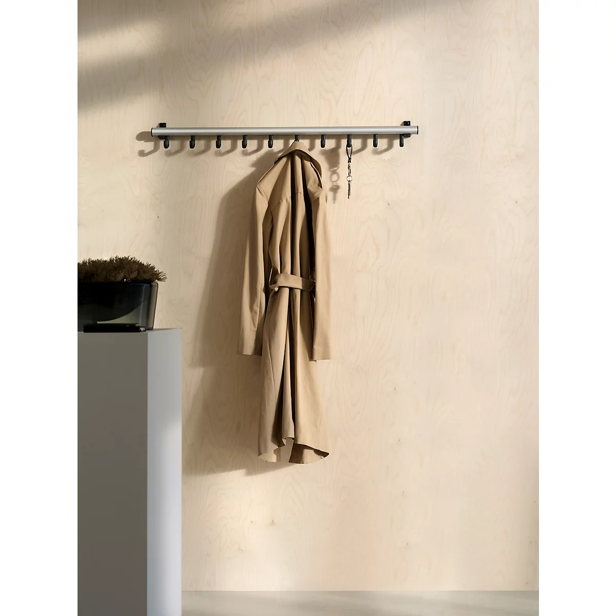Wandrek. Bruine trenchcoat hangt aan haken, sleutels ernaast.
