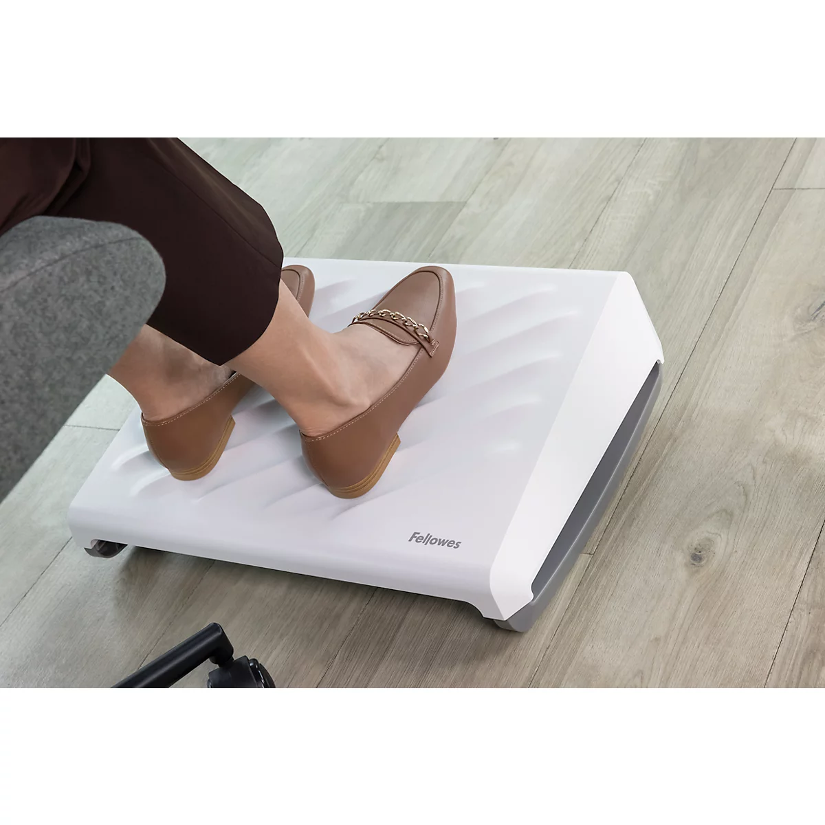 Person benutzt eine weiße Fußstütze mit Füßen in braunen Schuhen. Das Fellowes-Logo ist sichtbar.