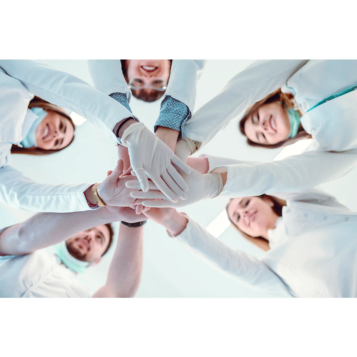 Équipe médicale en cercle, mains jointes, en blouses blanches et gants, souriant.
