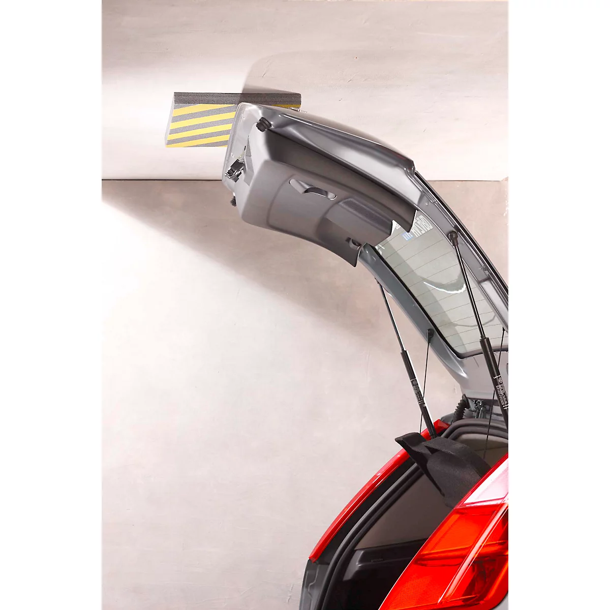 Open tailgate of a car. In the garage, a protector for the ceiling with yellow and black stripes.