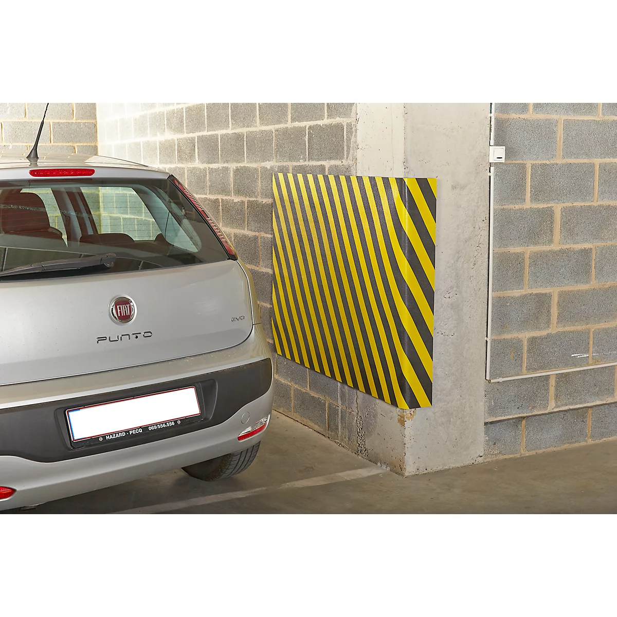 Ein silberner Fiat Punto parkt in einer Garage neben einem gelb-schwarz gestreiften Wandprotektor. Der Hintergrund besteht aus Betonblöcken.