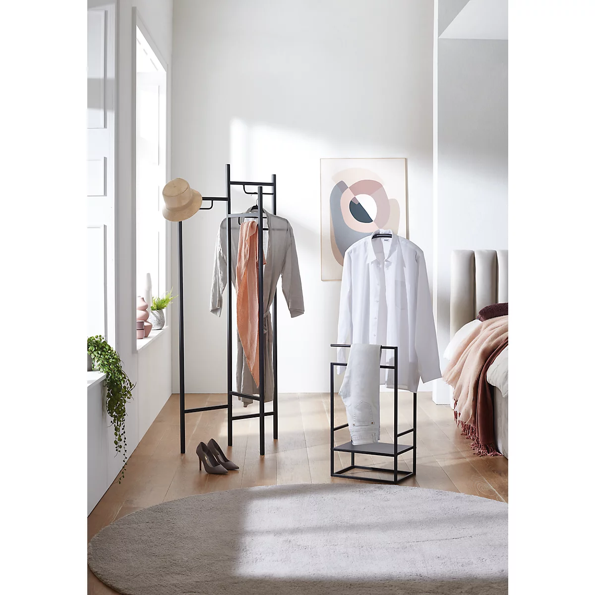 Schwarze Garderobe mit Kleidung und Accessoires in hellem Raum. Ein Hut, eine Schal, Schuhe und ein Teppich sind zu sehen.