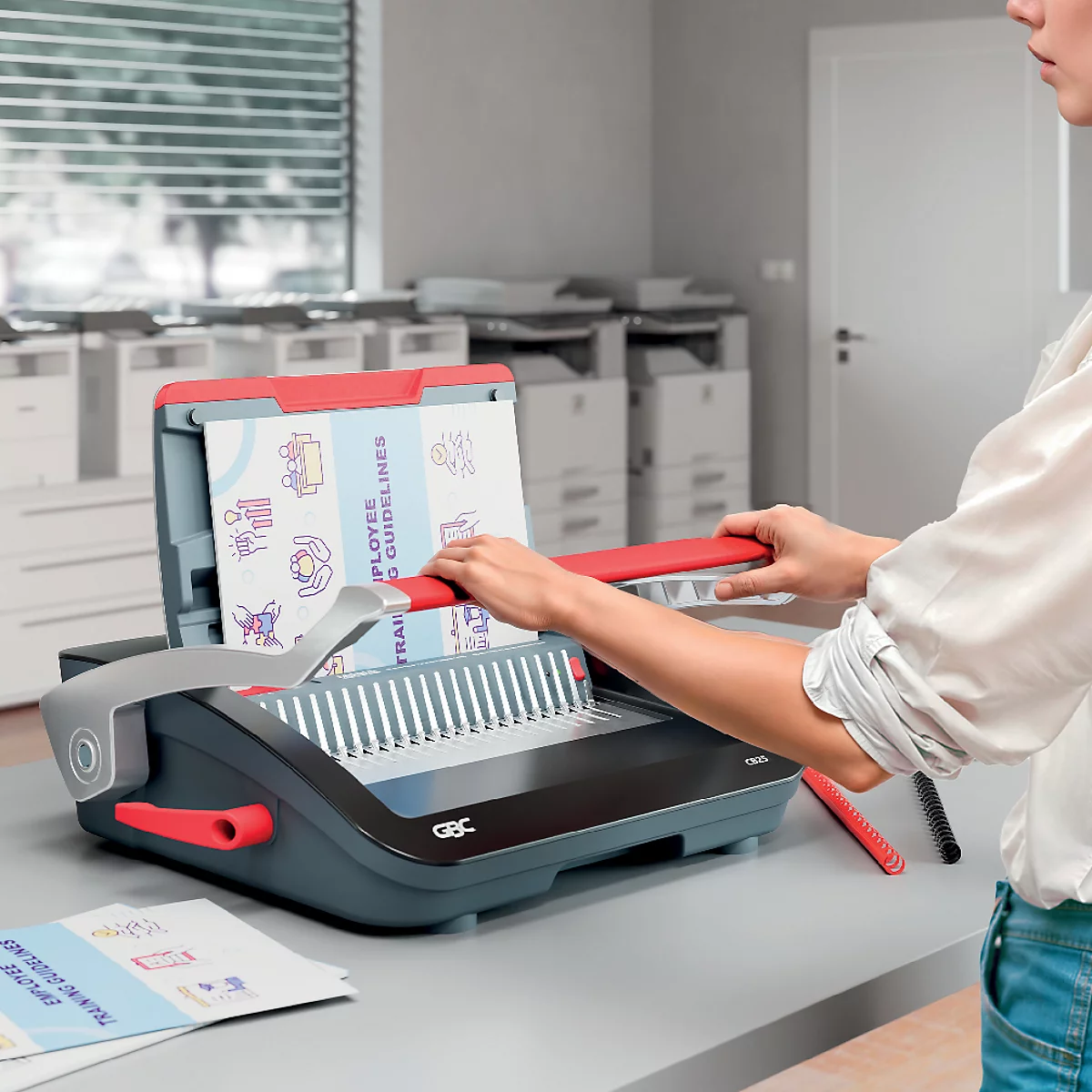 Persoon die documenten bindt op kantoor. Rode en grijze bindmachine. Op het papier staat: EMPLOYEE GUIDELINES.
