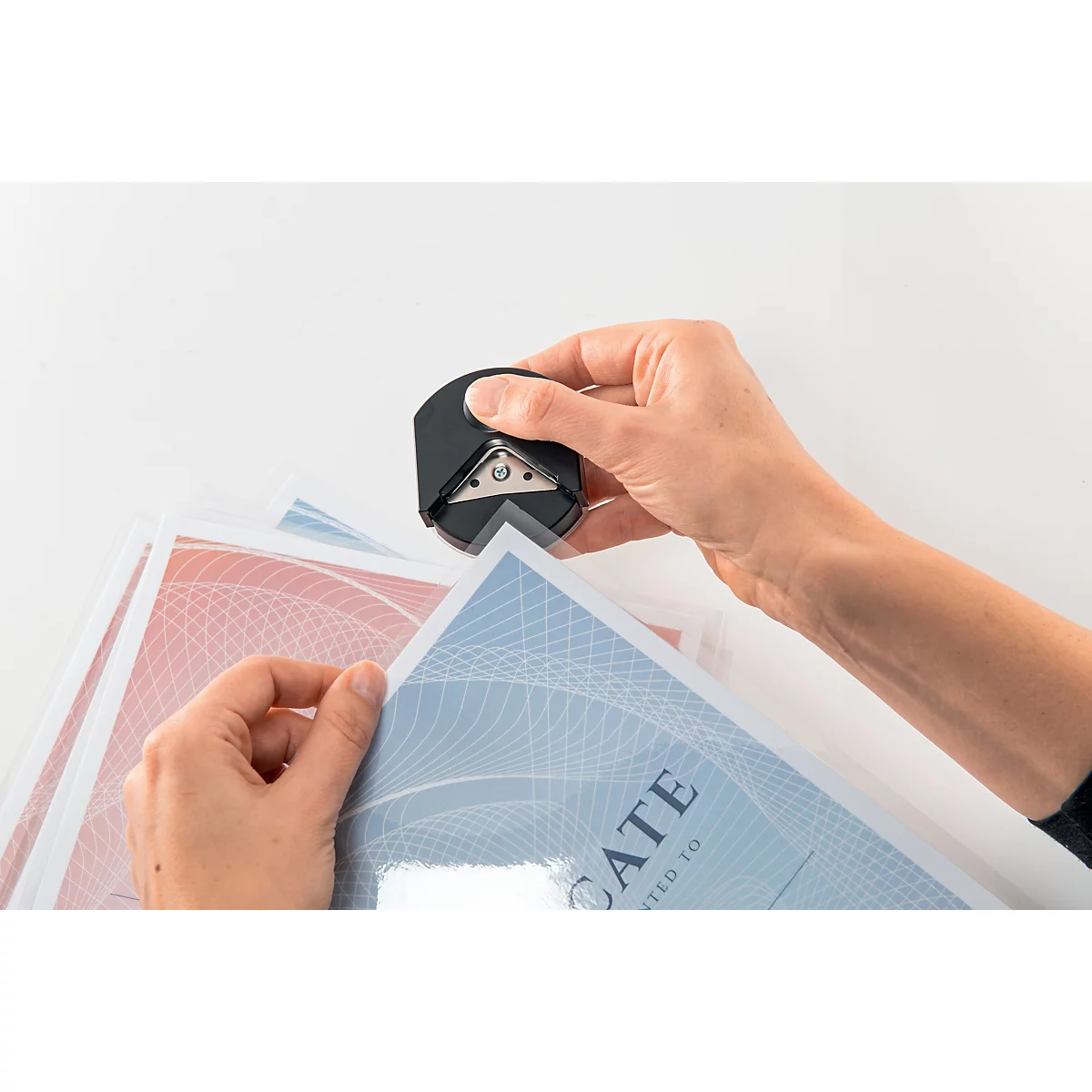 Handen gebruiken een zwarte hoekronder om papier te snijden. Op de papieren zijn blauwe en rode patronen te zien.