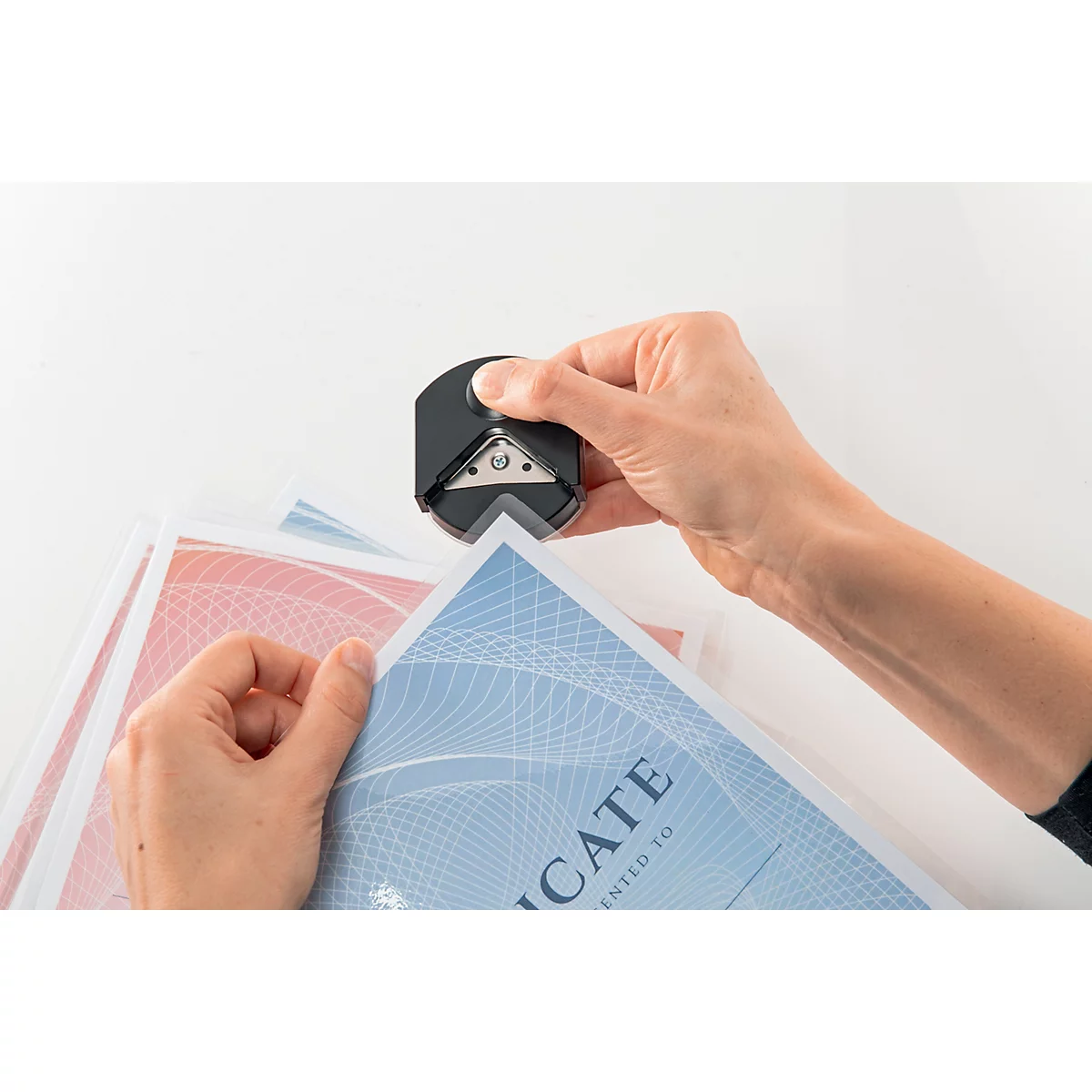 Handen die hoeken afronden van papier met blauwe en rode achtergronden. Een hoeksnijder wordt bediend.