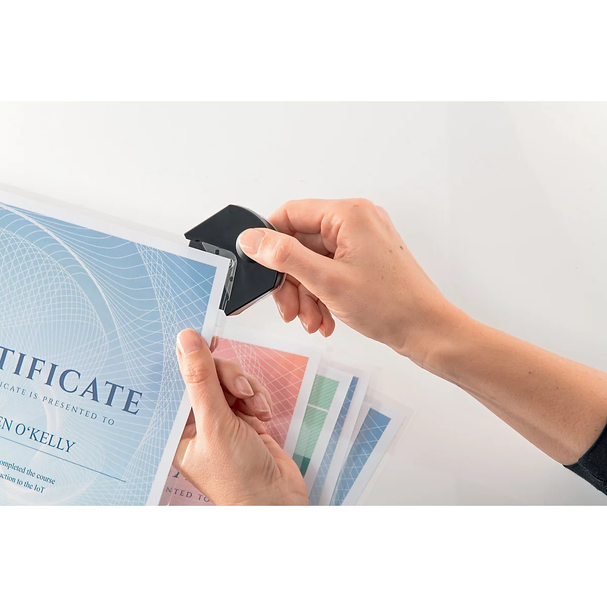 Mains utilisant un arrondisseur d'angle noir pour découper des certificats. Modèle de certificat bleu avec le mot "Certificate".