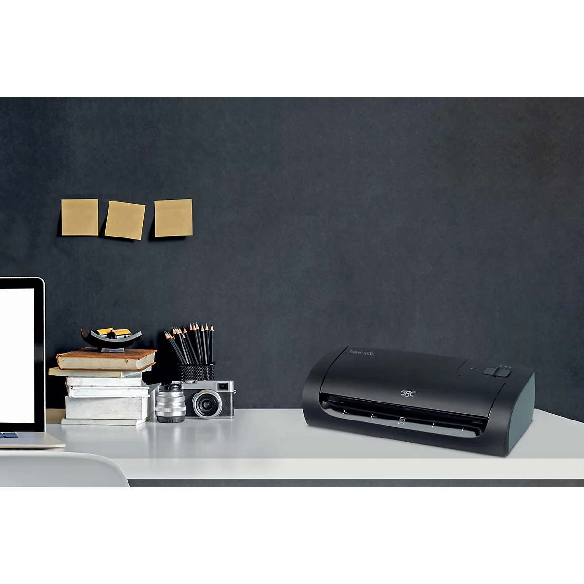 Laminateur noir sur un bureau blanc avec ordinateur portable, stylos et notes.