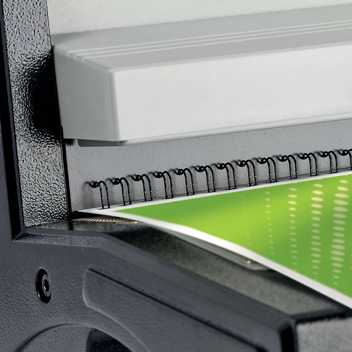 Gros plan d'une relieuse noire reliant un document avec un fond vert. Il y a une partie blanche en haut.
