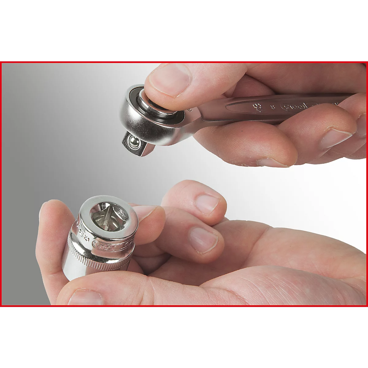 Nahaufnahme von Händen, die eine Ratsche und eine Stecknuss halten. Der obere Teil der Ratsche ist in der Nähe der Stecknuss.