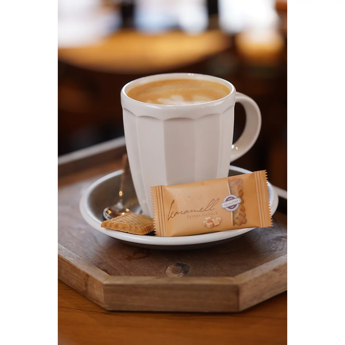 Eine cremige Tasse Kaffee in einer geriffelten Tasse mit einer Karamellwaffel auf einem Holztablett.