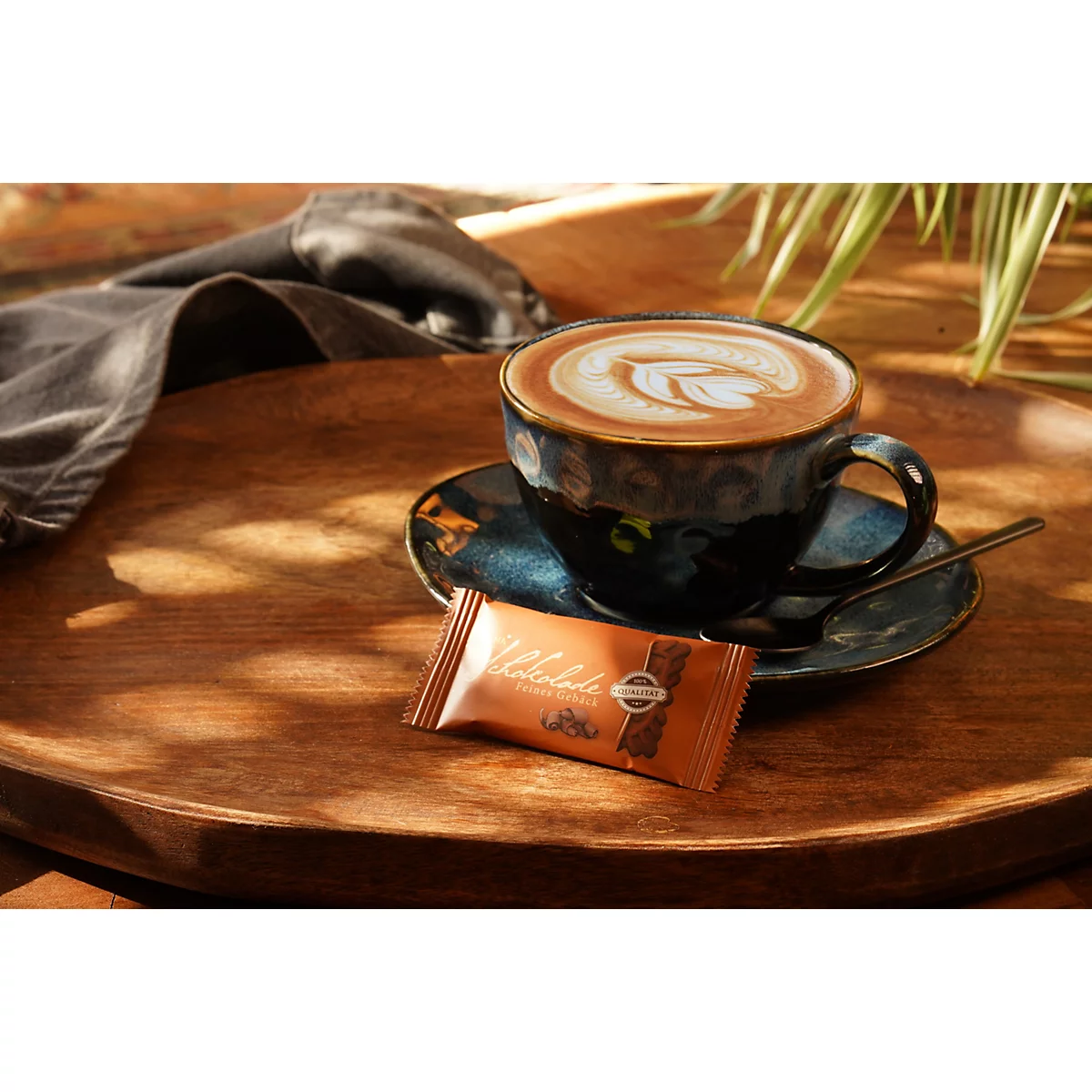 Tasse Kaffee mit Latte Art und kleiner Schokoriegel auf einem hölzernen Tablett.