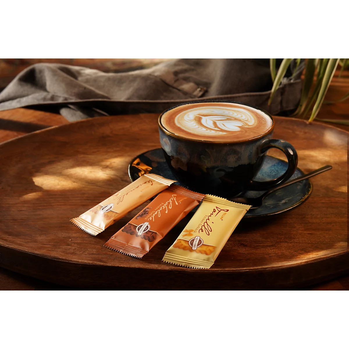 Eine Tasse Cappuccino mit Latte Art und drei verschiedenen Gebäckriegeln auf einem Holztablett.