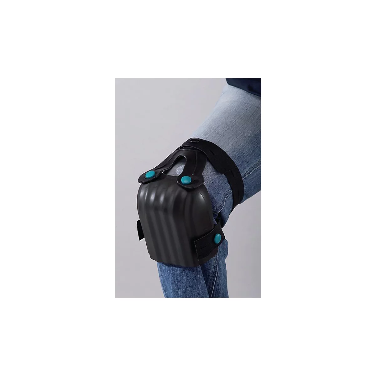 Genouillères sur une jambe. Les coussinets noirs sont fixés avec des boutons bleus et des sangles noires. Le porteur porte un jean.