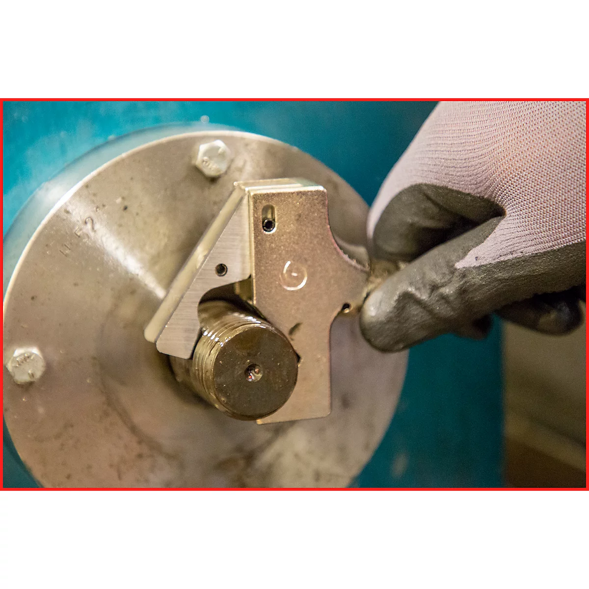 Ein Arbeiter in grauem Handschuh kontrolliert ein metallisches Werkstück mit einem Messwerkzeug.