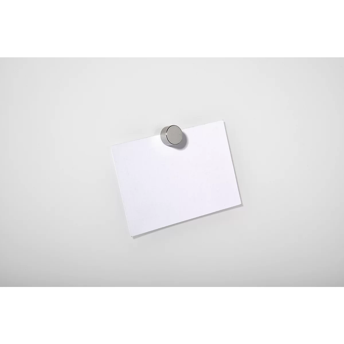 A white memo pad, attached to a white surface with a round, silver magnet.