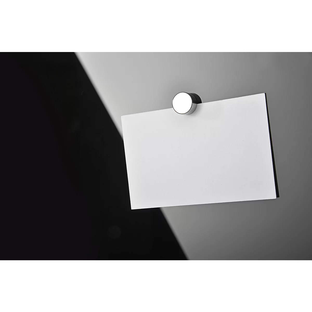 A white sheet of paper attached to a gray surface with a magnet, in front of a black background.