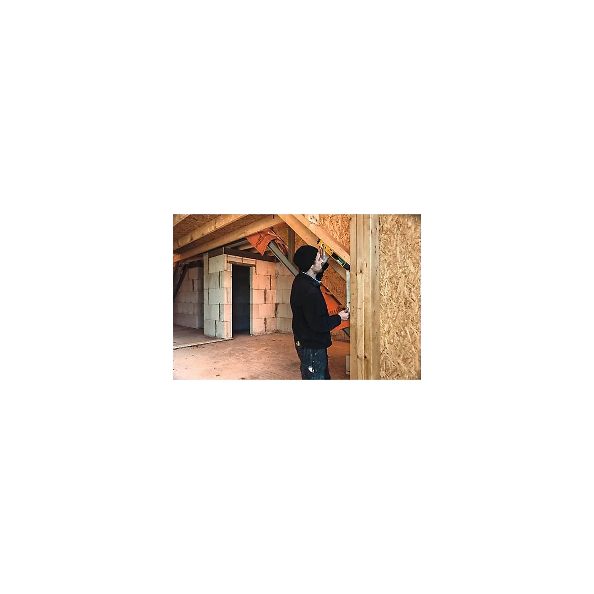 Un homme en tenue de travail, avec un niveau à bulle, dans une construction brute.