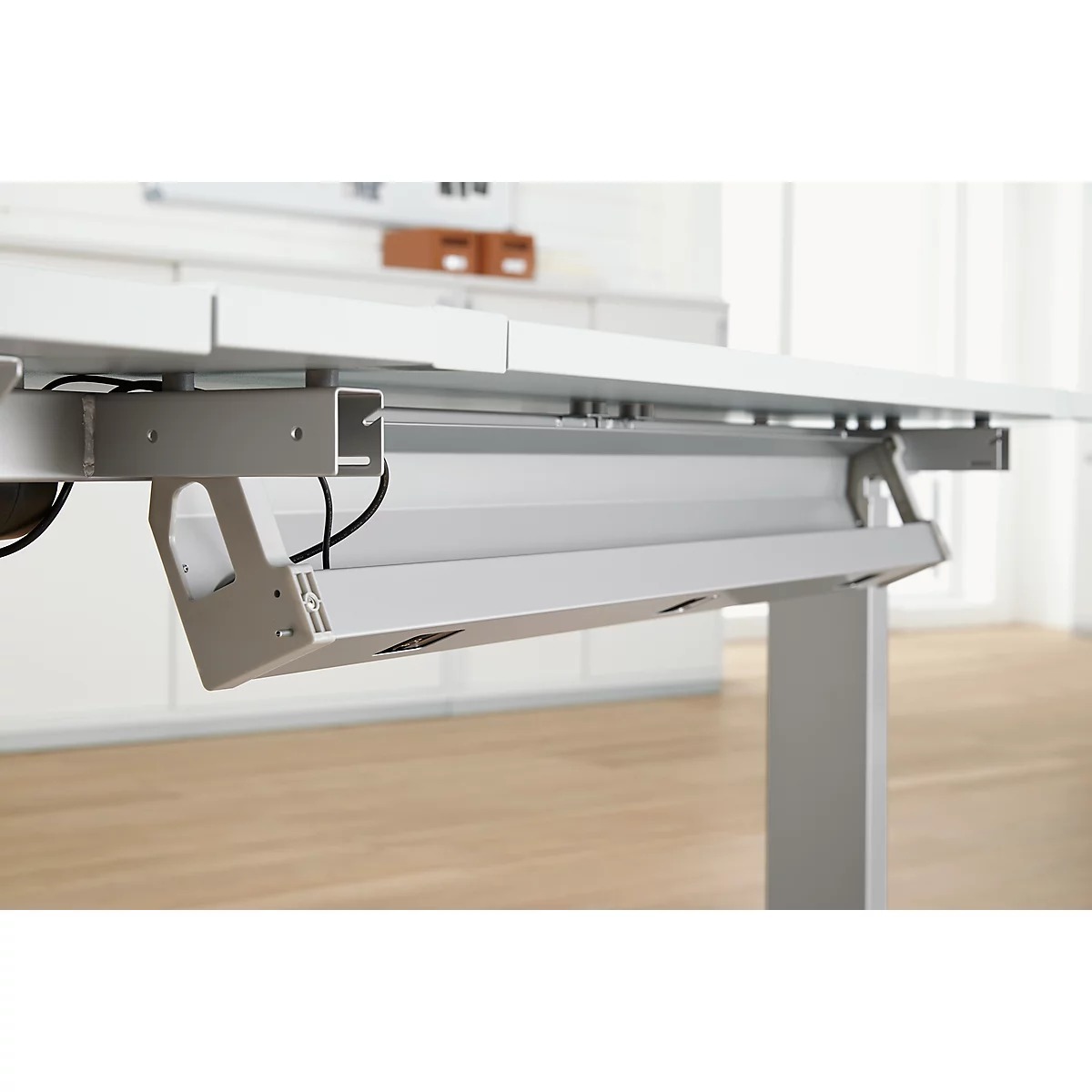 Gros plan sur le dessous blanc d'un bureau. Un bac métallique pour câbles est situé sous la table.