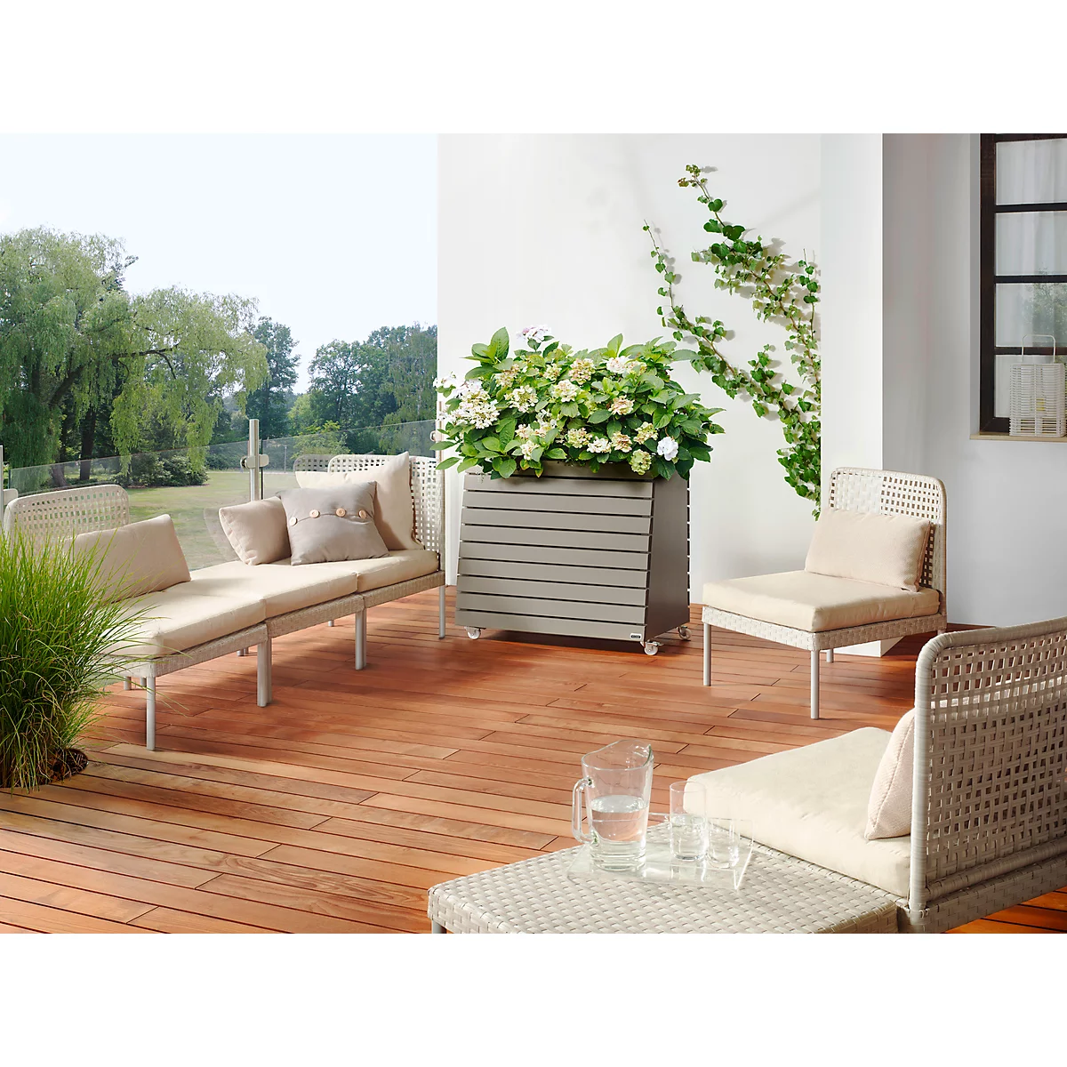 Terras met houten vloer, tuinmeubelen, bloembak en planten op de achtergrond. Een uitnodigende scène.