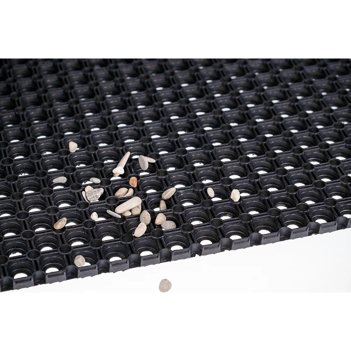Schwarze Gummi-Lochmatte mit quadratischer Struktur, auf der kleine Kieselsteine liegen.