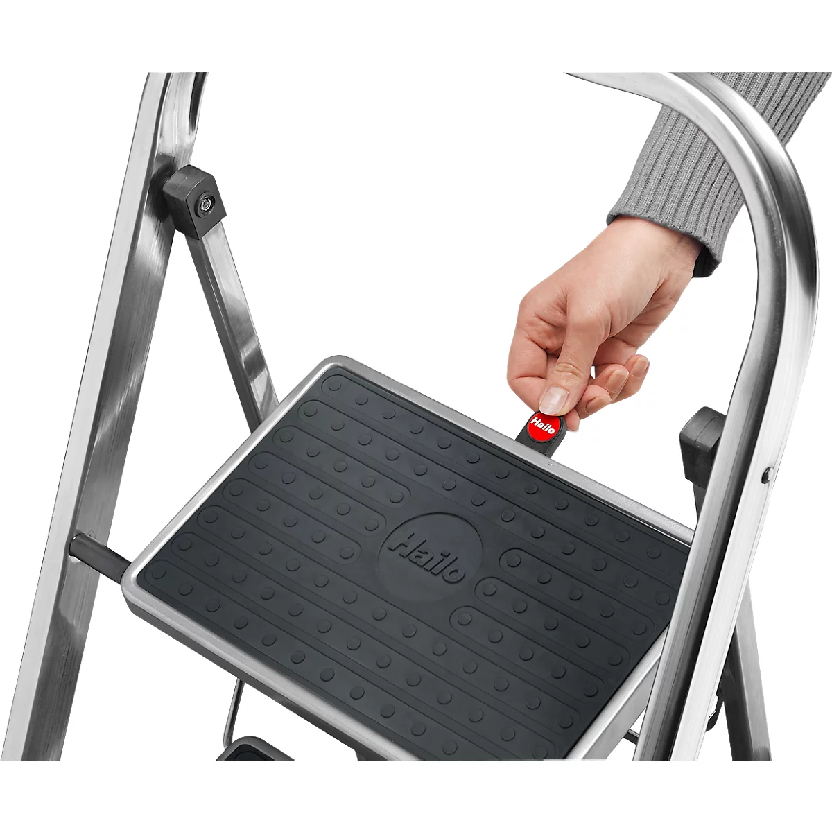 Hand operating red safety lock on step ladder. Gray ladder, black tread with 'Hailo' logo.