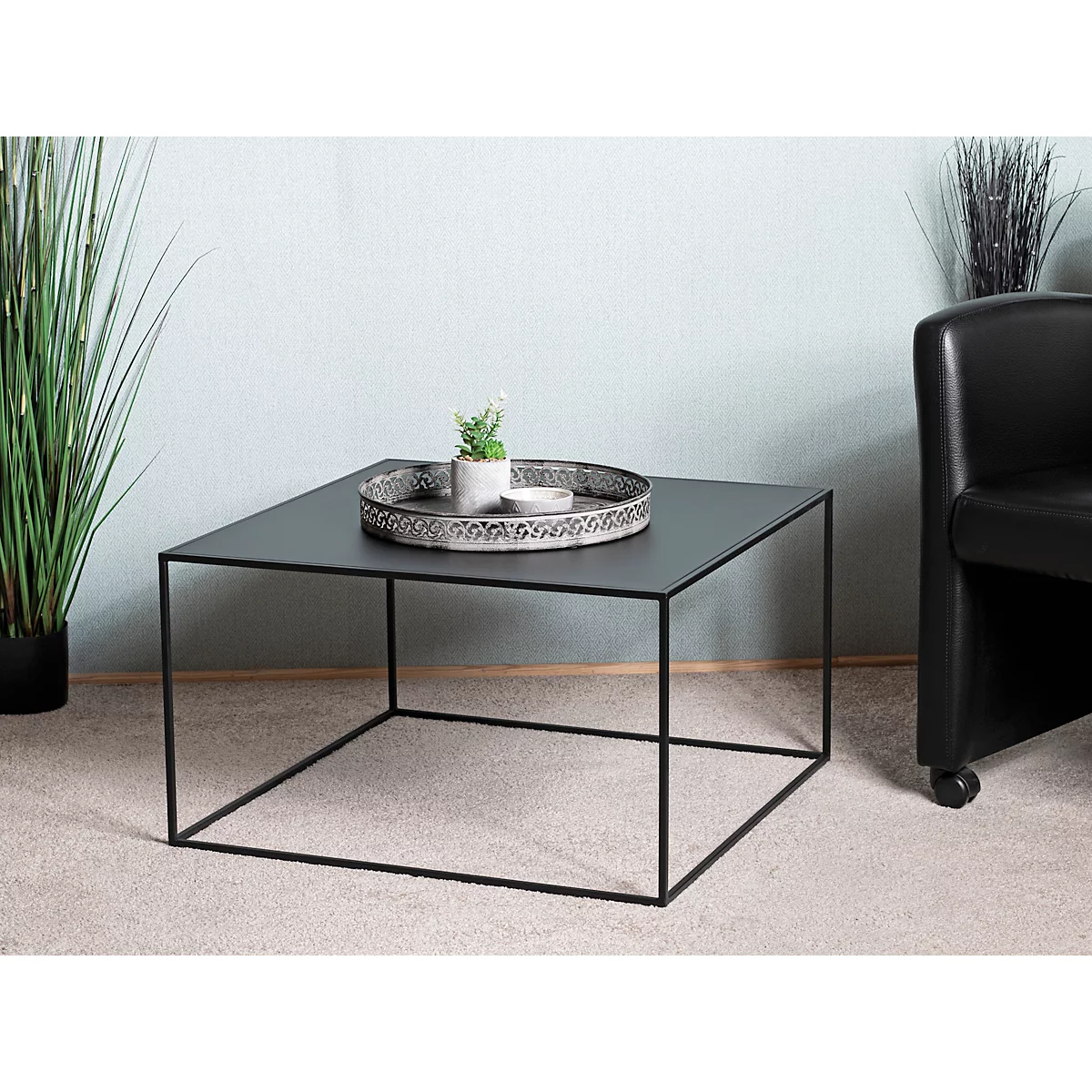 Vierkante zwarte salontafel met dienblad en plant. Achterin een zwarte fauteuil.