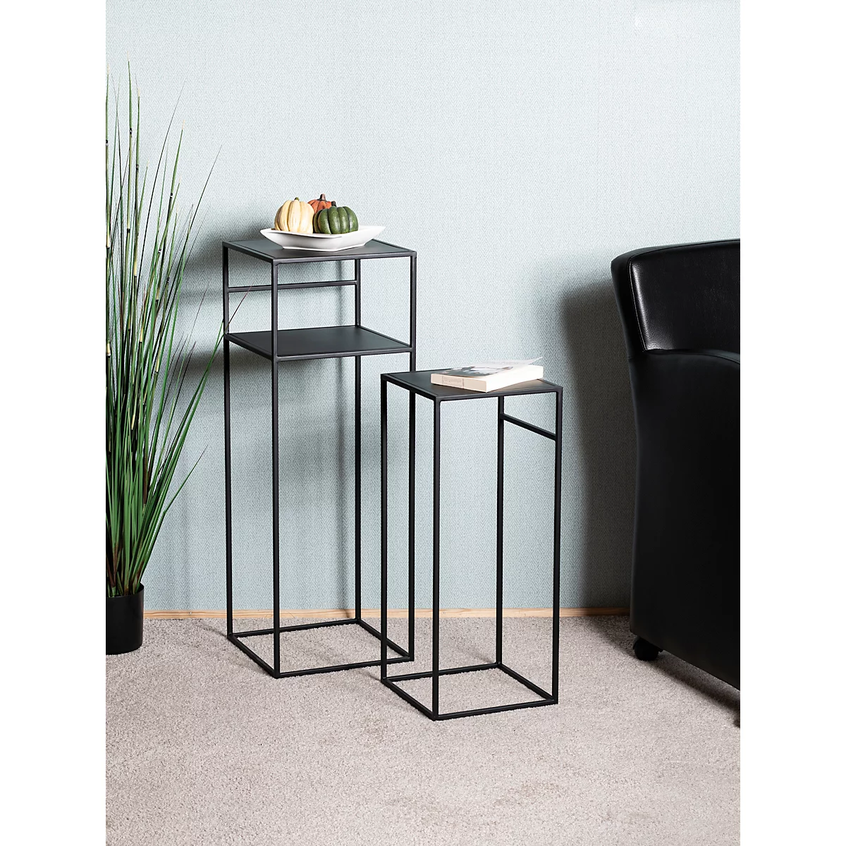Deux supports de plantes en métal noir. Sur l'un se trouve un livre, sur l'autre des citrouilles décoratives sur une assiette.