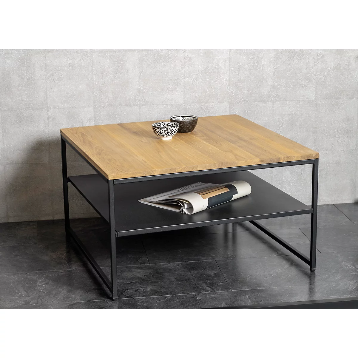 Table basse carrée avec plateau en bois, cadre noir et étagère. Deux bols, des magazines sont prêts.