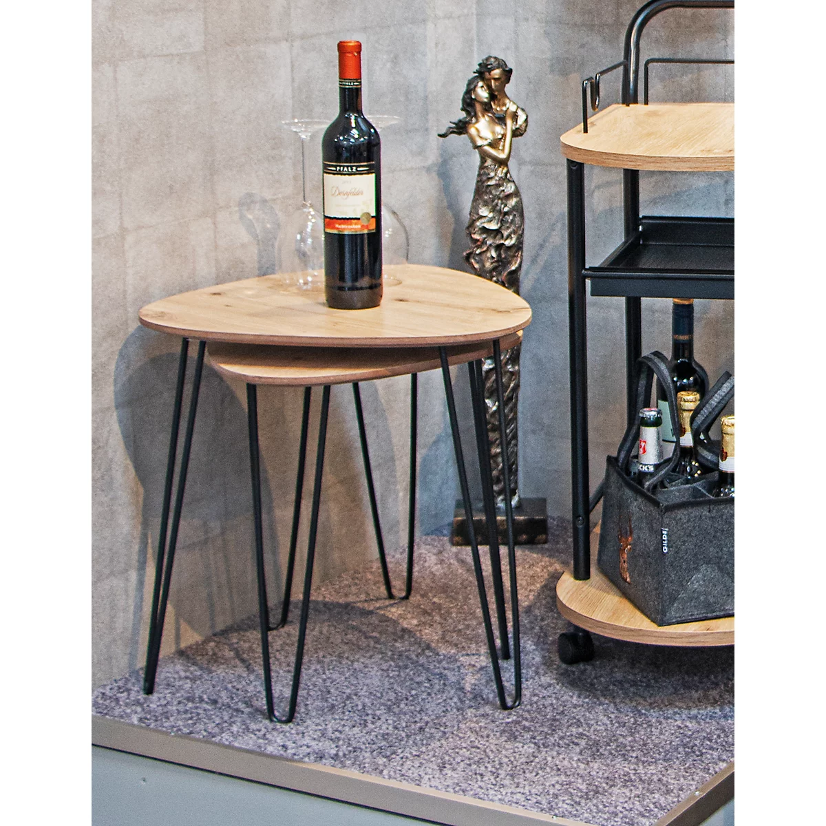 Deux tables d'appoint rondes avec des pieds noirs et une bouteille de vin. Une sculpture et un chariot de service en arrière-plan.