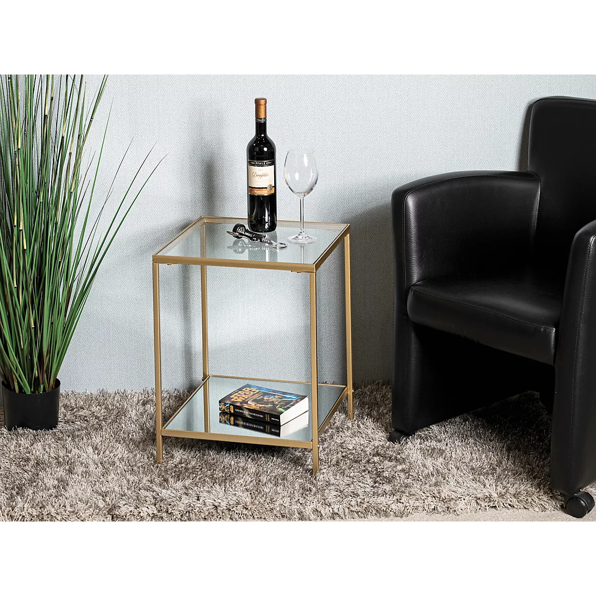 Table d'appoint avec plateau en verre et cadre doré, sur laquelle se trouvent une bouteille de vin, un verre à vin et un livre.
