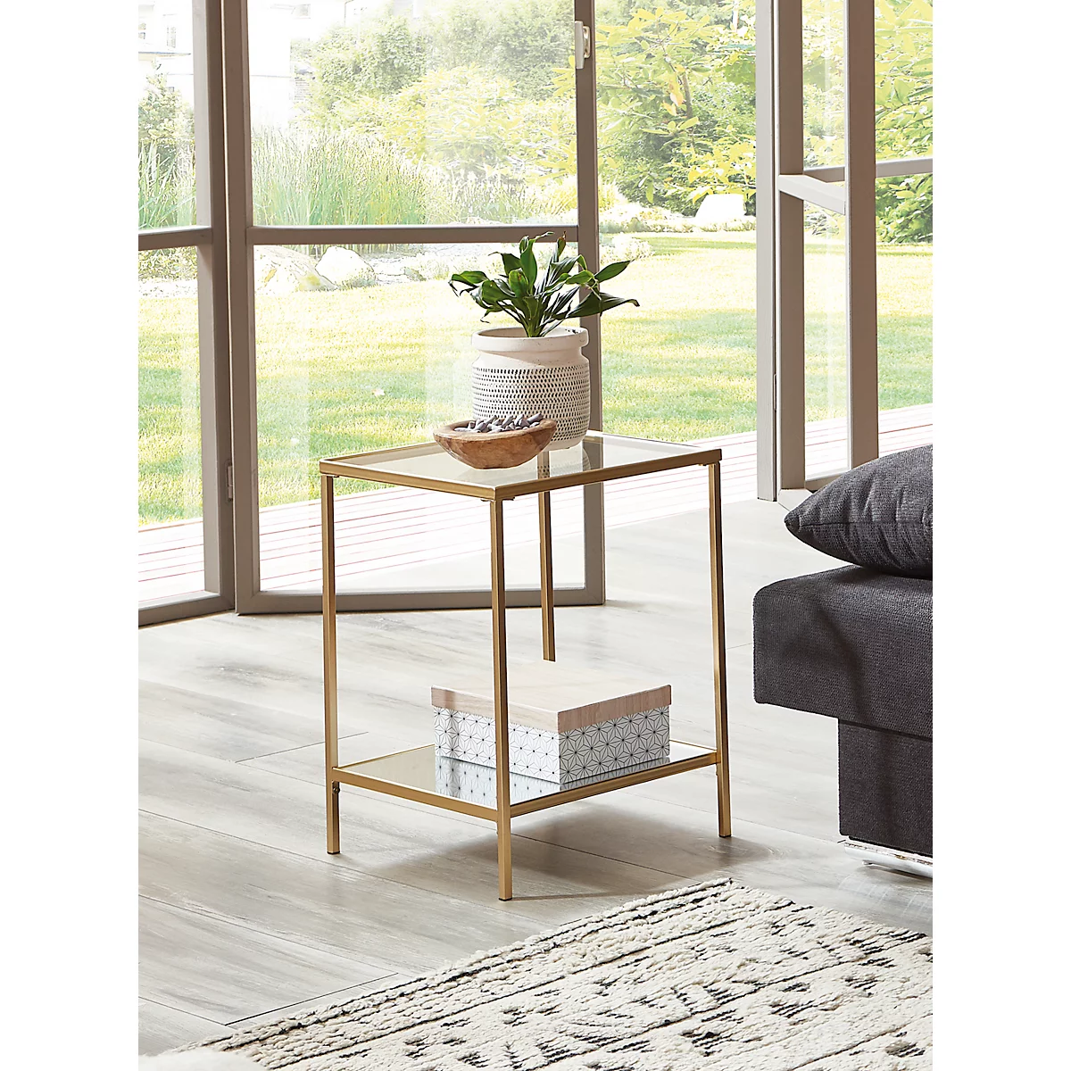 Table d'appoint avec plateau en verre, cadre doré, plante, bol, boîte. Devant la fenêtre, canapé à gauche.