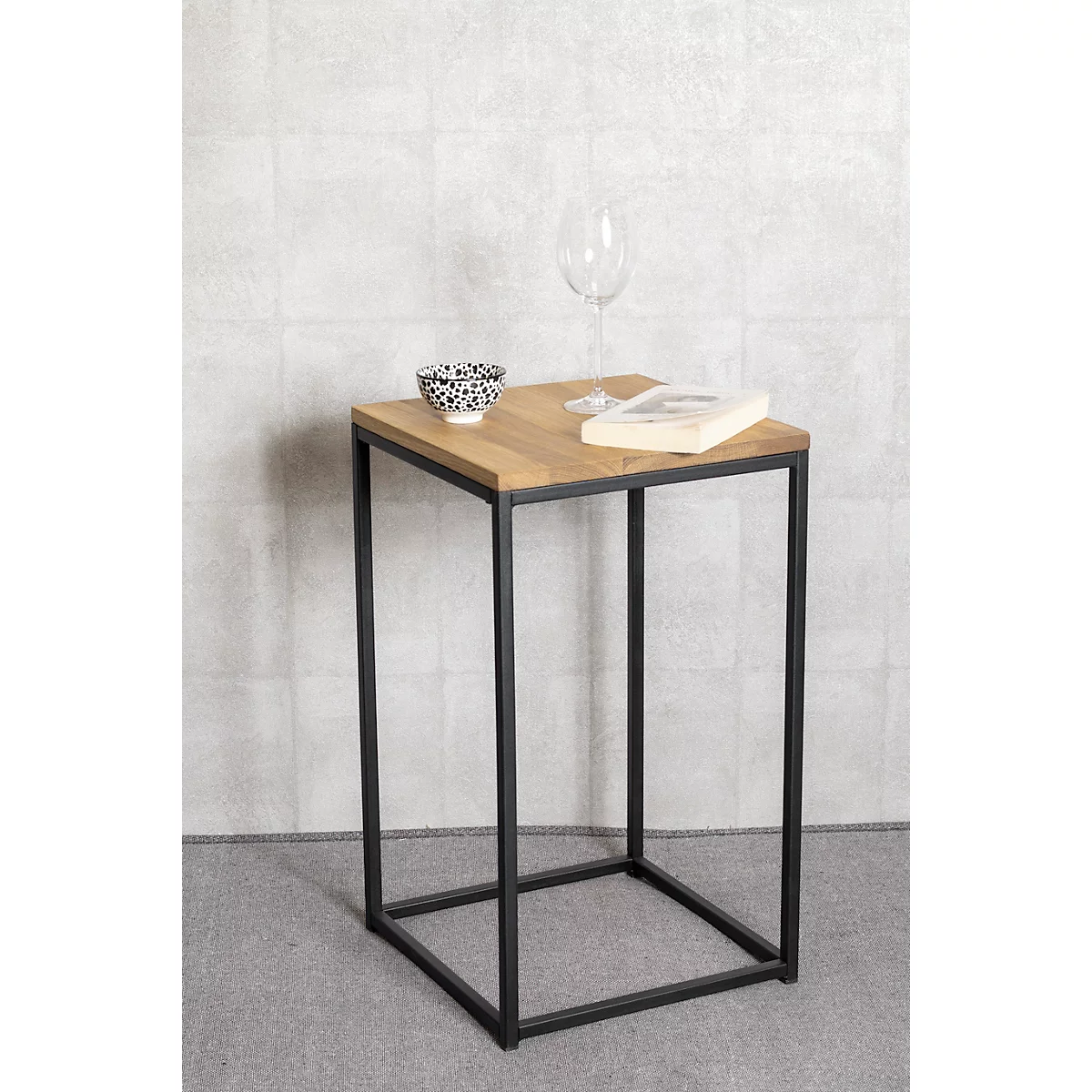 Table d'appoint avec plateau en bois, cadre en métal noir, verre, bol et livre. Fond gris.
