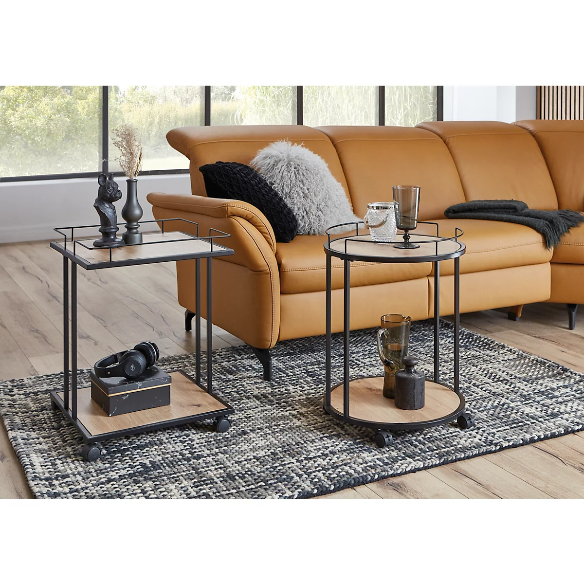 Deux tables d'appoint avec plateaux en bois et cadres en métal noir. Des verres sont posés sur la table de droite, le fond montre un canapé ocre.