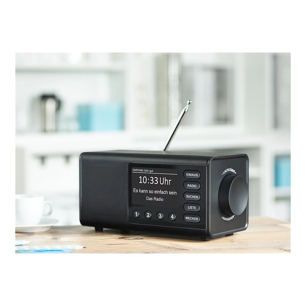 Radio noir sur une table en bois, heure 10h33, texte sur l'Ã©cran. Antenne, boutons et une commande rotative.