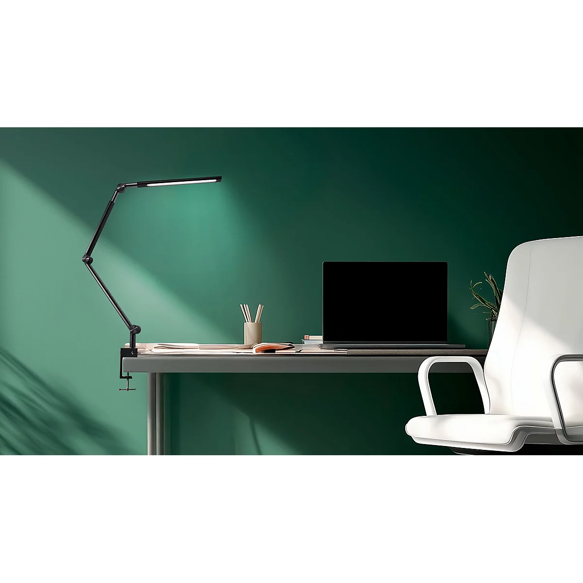 Schreibtisch mit Lampe, Laptop und Stuhl vor grüner Wand. Die Lampe beleuchtet den Tisch. Ein heller Fleck erhellt die Szene.