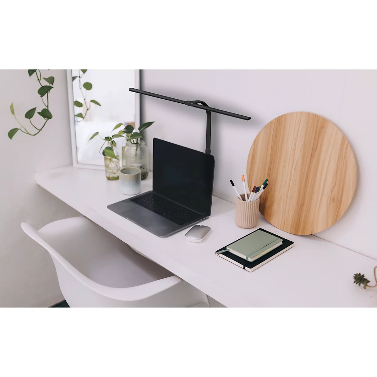 Ein minimalistischer Schreibtisch mit Laptop, Lampe, Notizbuch und Holzbrett.