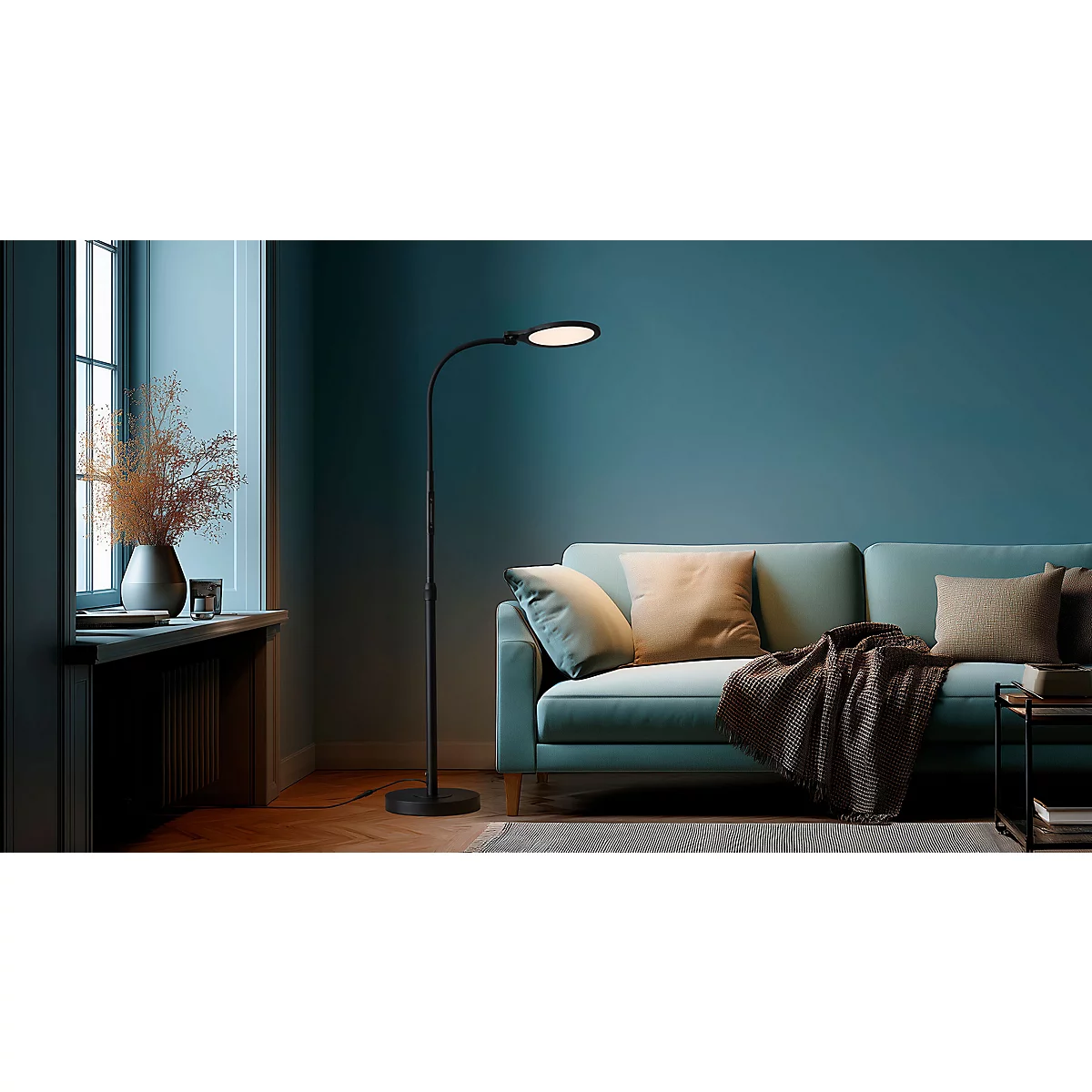 Zwarte vloerlamp verlicht woonkamer. Naast bank, raam met planten en kussens.