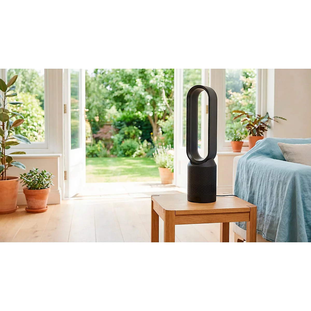 Zwarte torenventilator op houten tafel. Achtergrond: tuin, bank, planten.