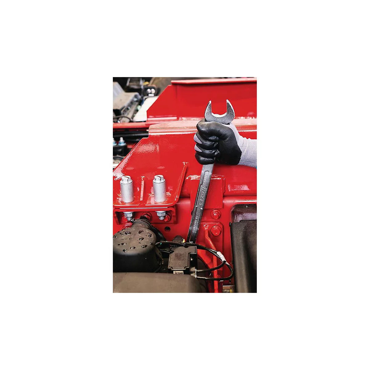 Gros plan d'une main gantée tenant une clé sur une pièce de machine rouge.
