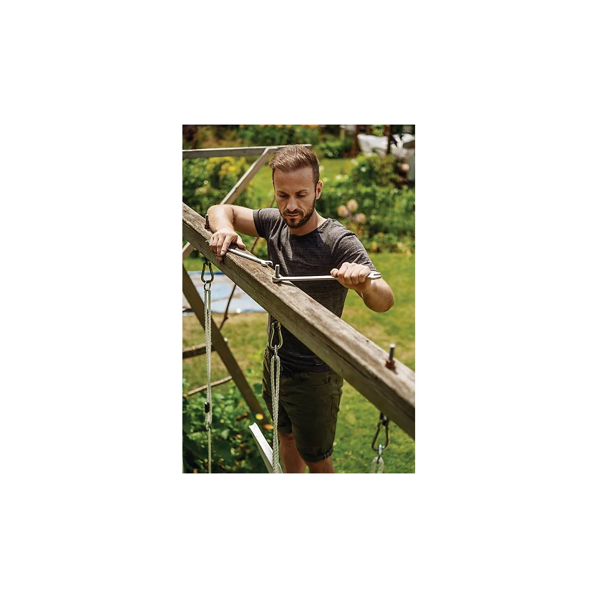 Man repareert houten frame in de tuin, met gereedschap. Groene struiken op de achtergrond.
